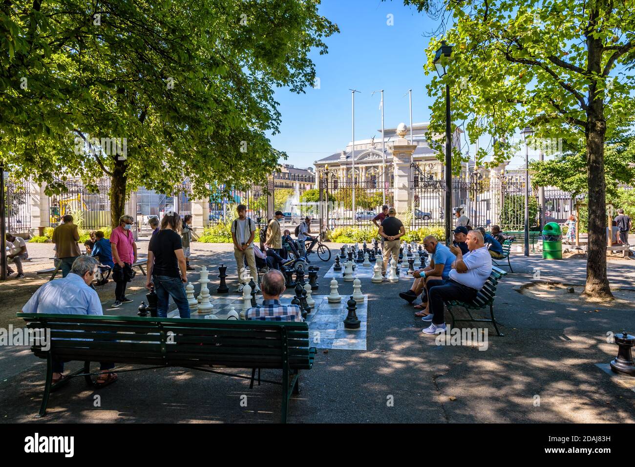 La gente gioca a scacchi su scacchiere giganti all'ombra del parc des Bastions di Ginevra, con spettatori seduti sulle panchine intorno. Foto Stock