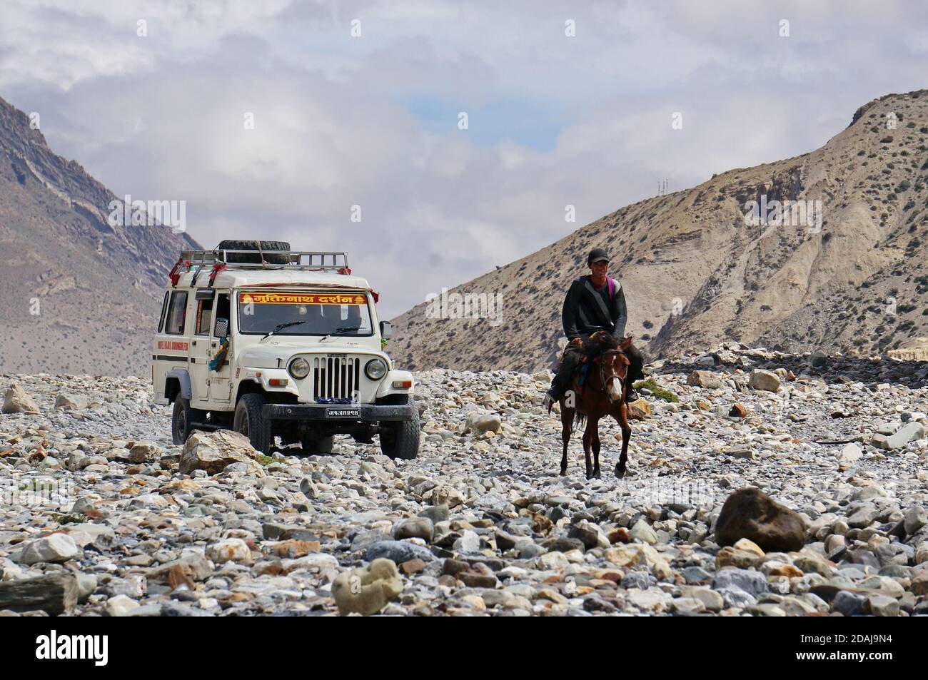 Una jeep turistica e un residente locale a cavallo Tra le montagne dell'Himalaya sulla strada per l'alta Mustang Foto Stock