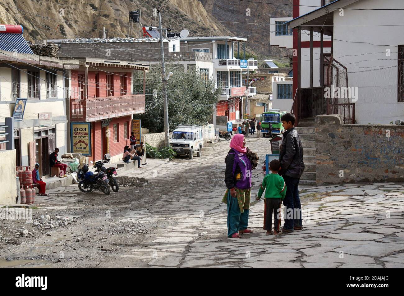 Una donna non identificata con un bambino che parla con un ragazzo sulla strada centrale di Jomsom in Nepal, distretto di Mustang. Foto Stock
