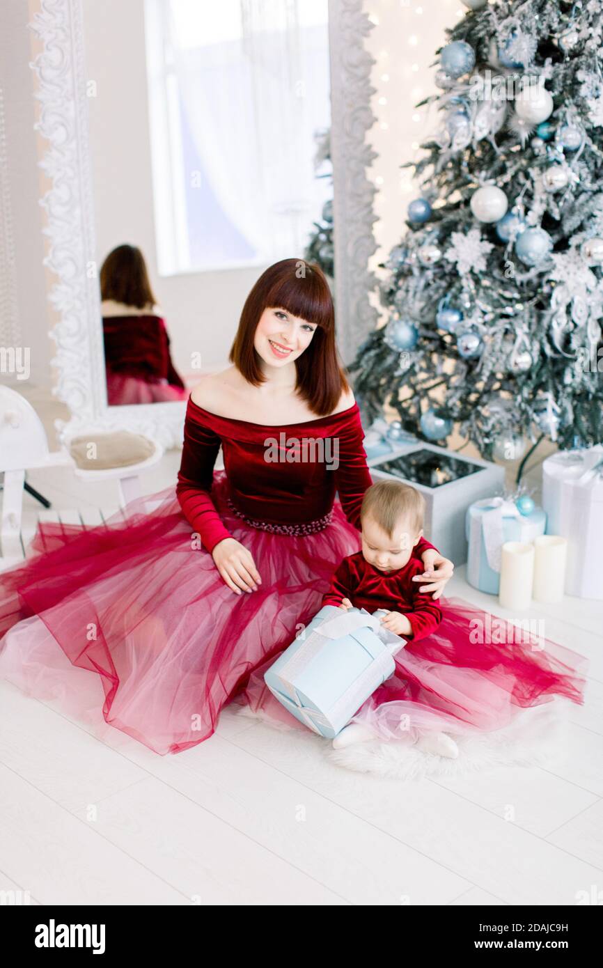 Bella giovane famiglia caucasaiana, madre con bambina, indossando eleganti abiti  rossi, seduto di fronte alle decorazioni natalizie e l'abete Foto stock -  Alamy