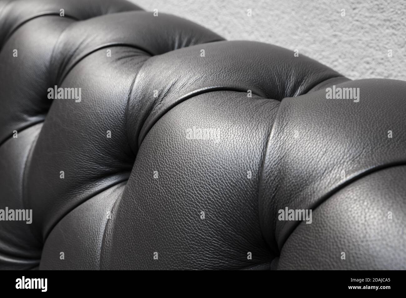 Il retro di un divano con morbida tappezzeria nera in pelle, primo piano con messa a fuoco morbida selettiva Foto Stock