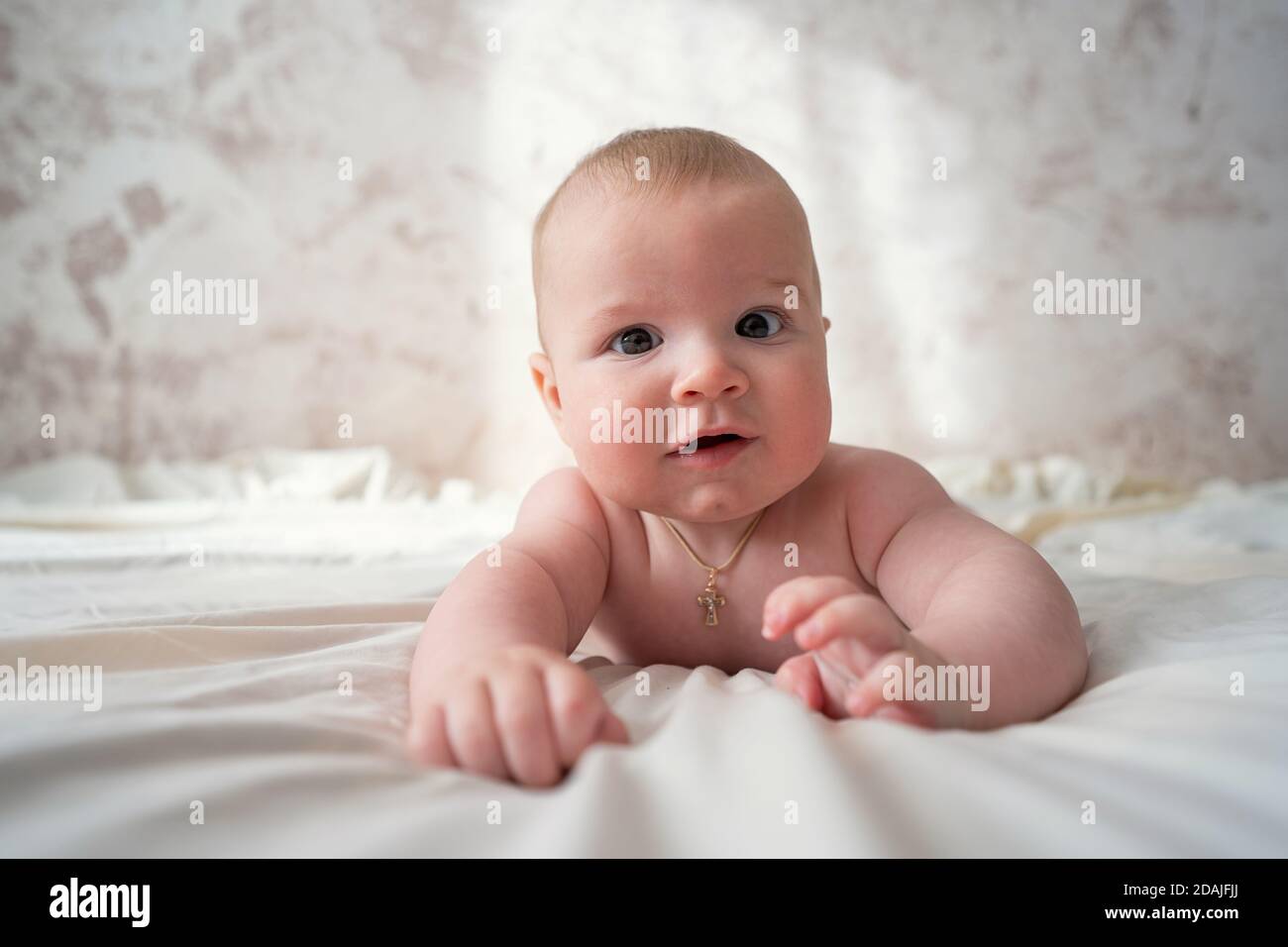 Carino bambino di sei mesi che giace sullo stomaco su un letto su uno sfondo beige. Messa a fuoco morbida, spazio di copia. Foto Stock
