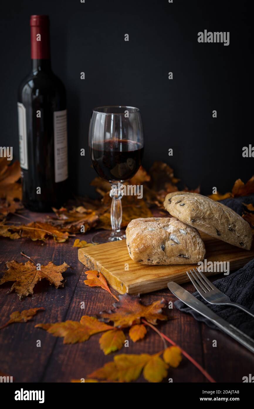 Vino rosso e pane su un tavolo con una dispersione di foglie d'autunno. Foto Stock
