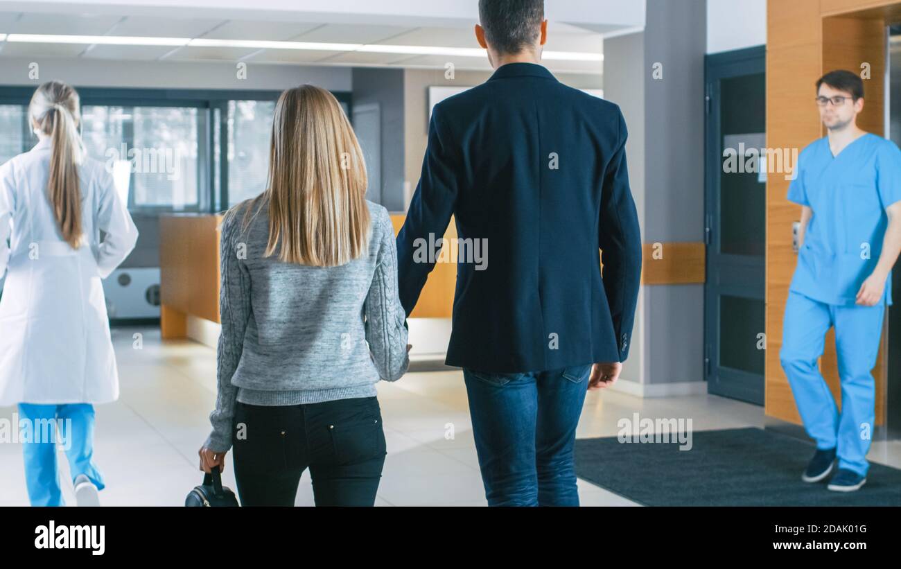 Nell'Ospedale giovani coppie passeggiate alla reception. Personale medico, Medici, infermieri, Assistenti e pazienti nella lobby Busy. Nuovo, moderno medico Foto Stock