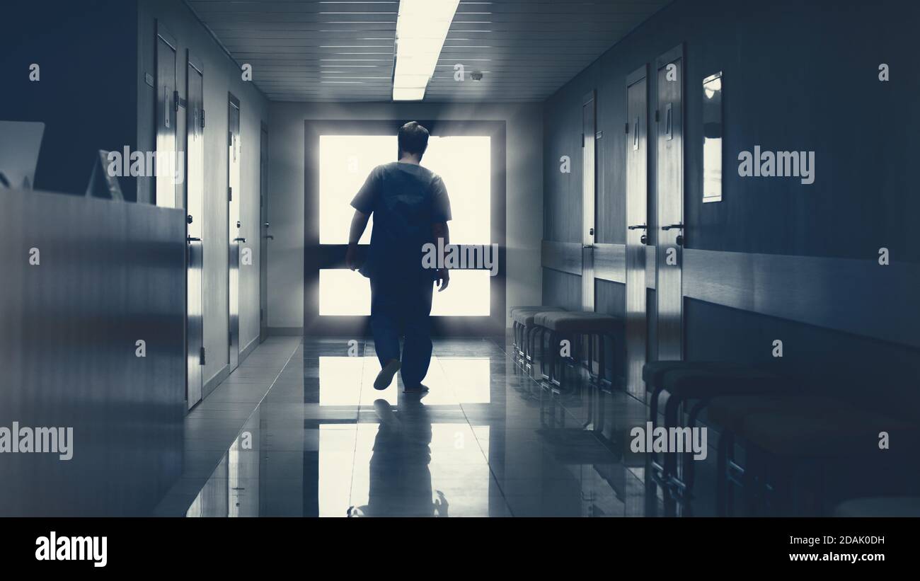 Nell'ospedale anziano uomo pensionato cammina lungo il corridoio con la luce alla fine. Struttura medica moderna e pulita. Vita dopo la morte, porta al cielo Foto Stock