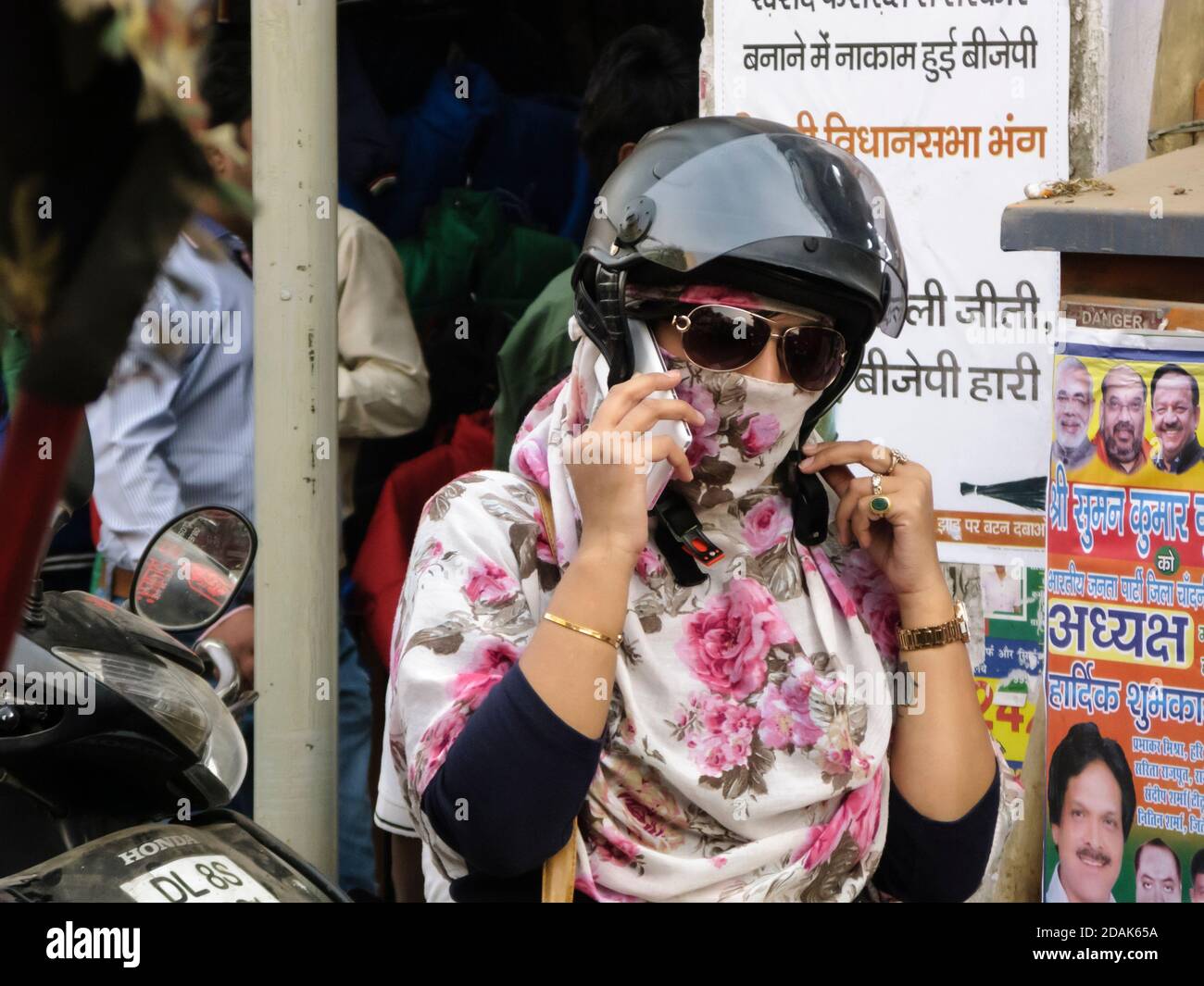 India, gastronomia. Una giovane e moderna donna sta per scendere su uno scooter. Mostra un tatuaggio sul braccio sinistro, smartphone, occhiali da sole, casco. Foto Stock