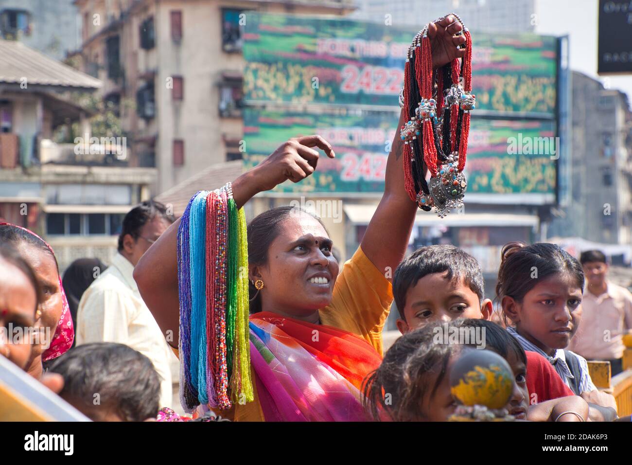 Una donna che tiene le collane ed i leis che sta provando a vendere sulla strada occupata s a Mumbai, India Foto Stock