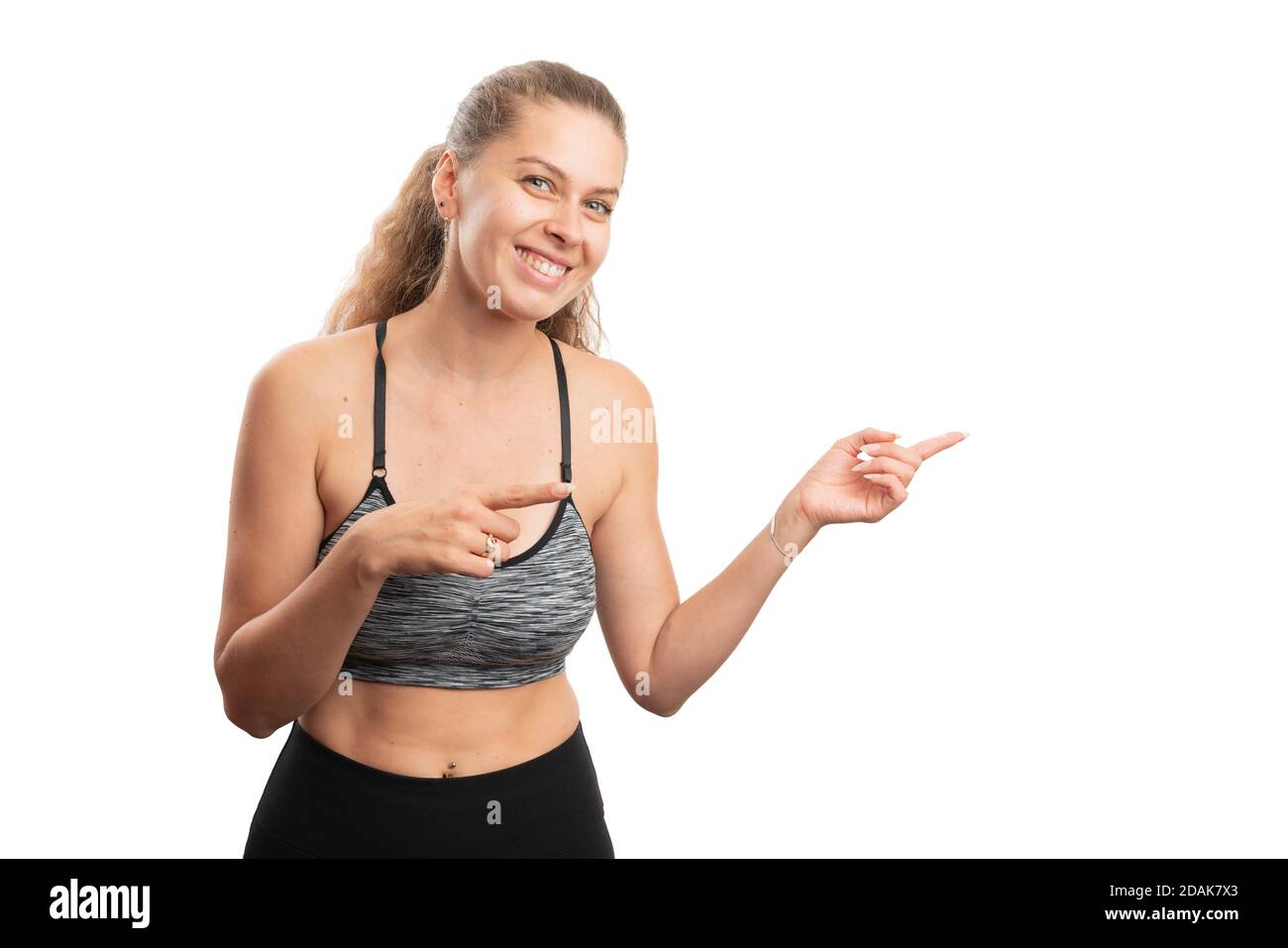 Donna adulta in forma che indossa abiti sportivi da allenamento sorridendo come puntamento indice dita a vuoto copyspace per la pubblicità di stile di vita attivo concetto isolato Foto Stock