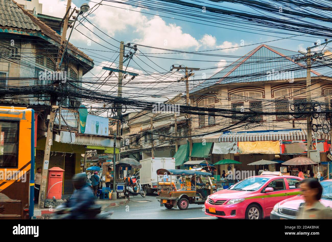 Stile di vita e ambiente di strada a Bangkok, Thailandia. Tuk tuk traffico, taxi rosa e autobus tradizionali. Groviglio di cavi elettrici e facciate di case Foto Stock