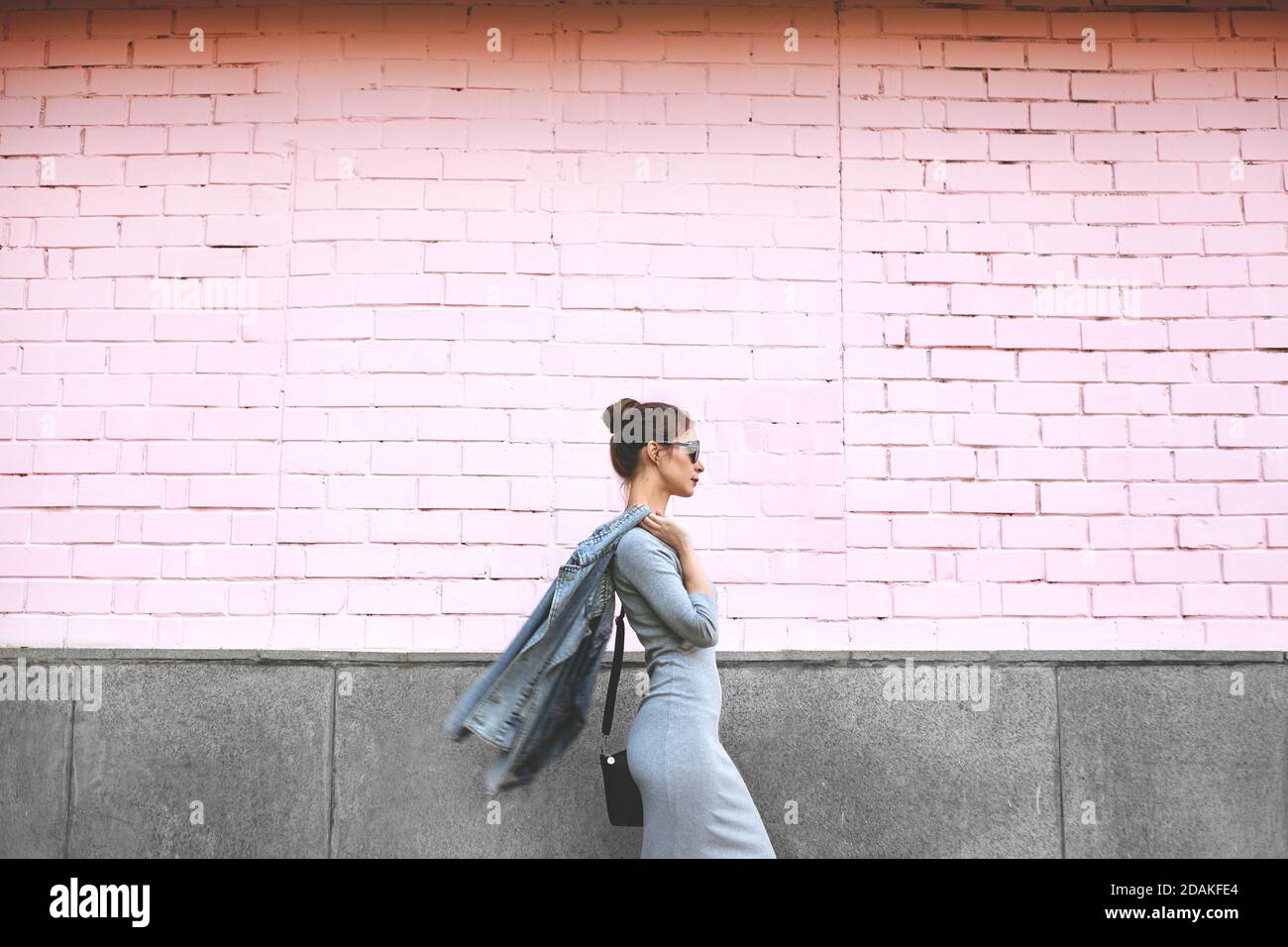 Stile di strada Shoot of Woman su parete rosa. Swag ragazza che indossa giacca Jeans, abito grigio, sunglass. Stile di vita all'aperto Foto Stock