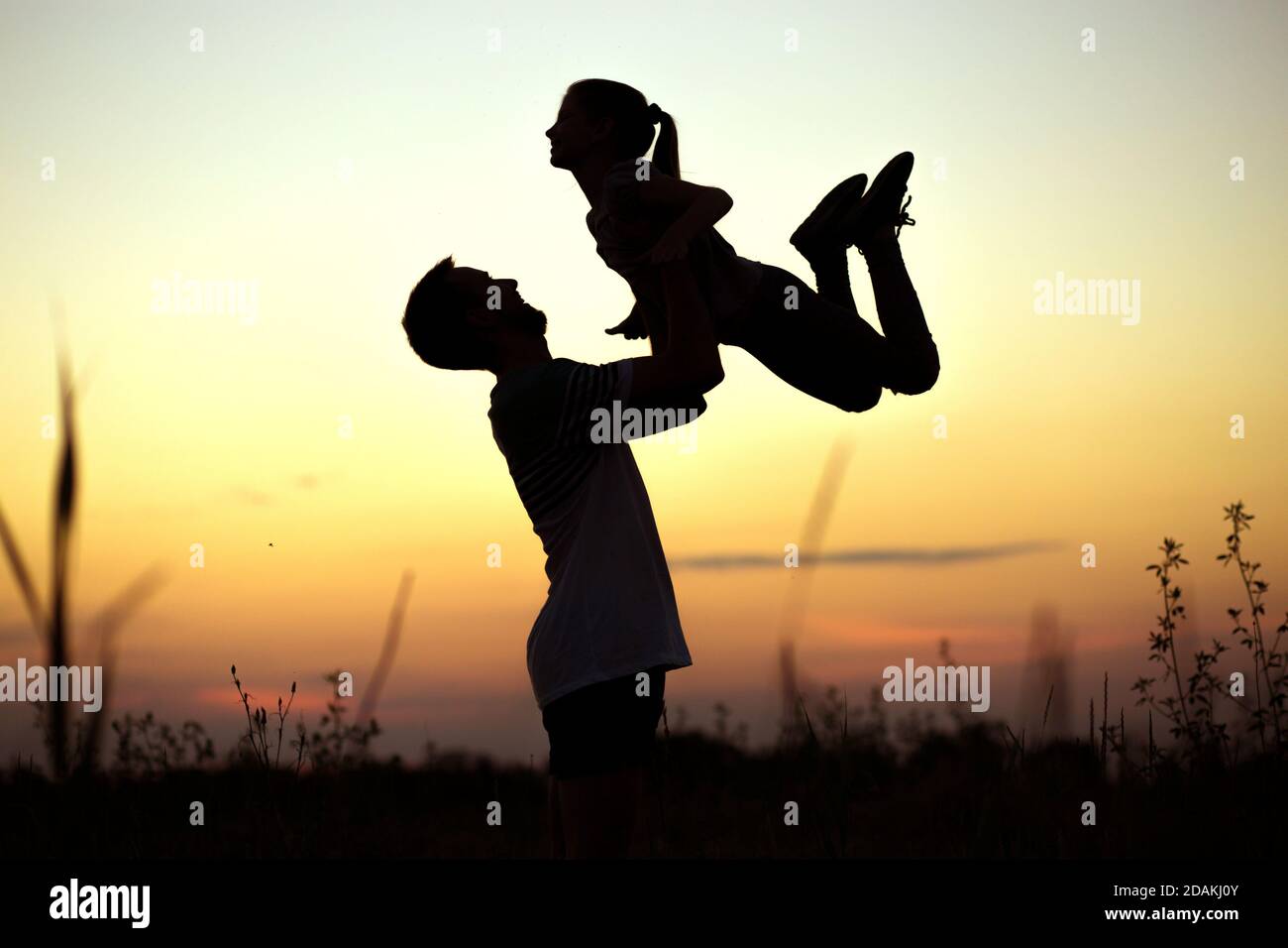 Silhouette di padre che getta la sua figlia felice nell'aria al tramonto. Famiglia togehter. Buon giorno del padre Foto Stock