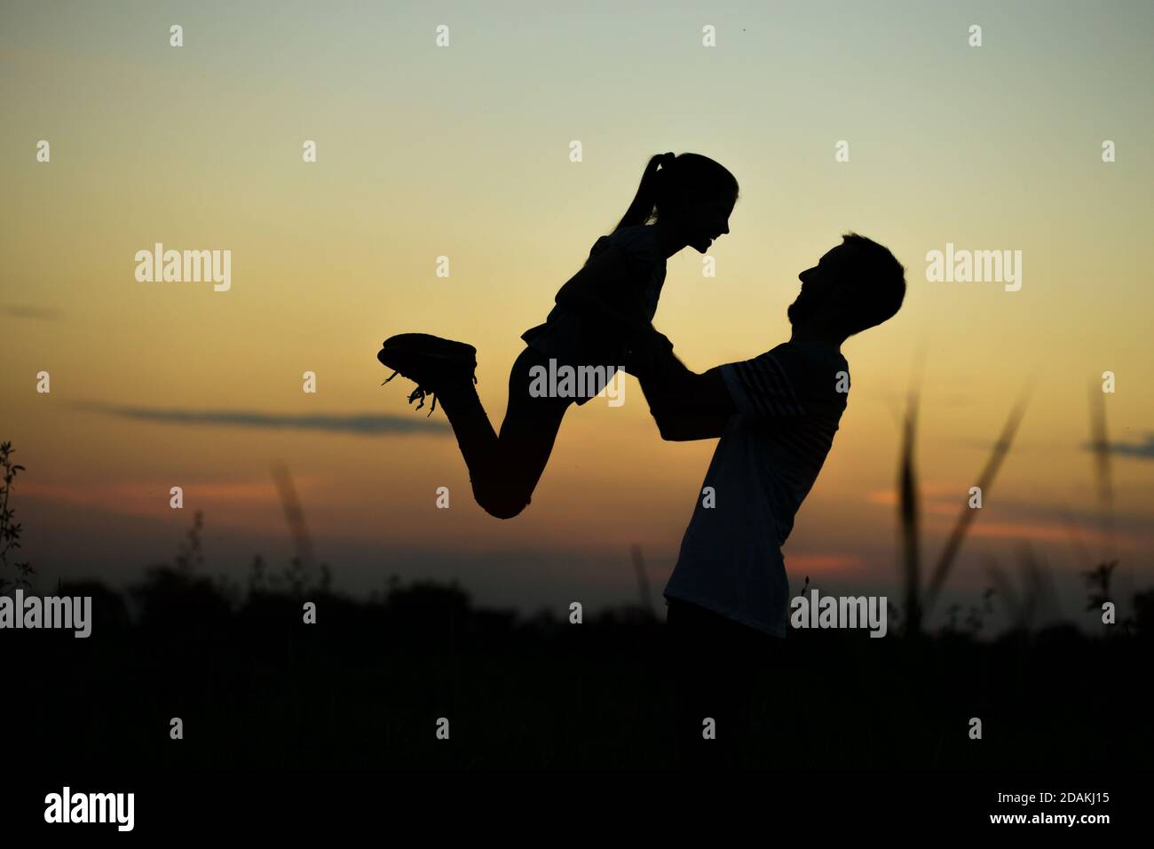 Silhouette di padre che getta la sua figlia felice in aria al tramonto. Famiglia togehter Foto Stock