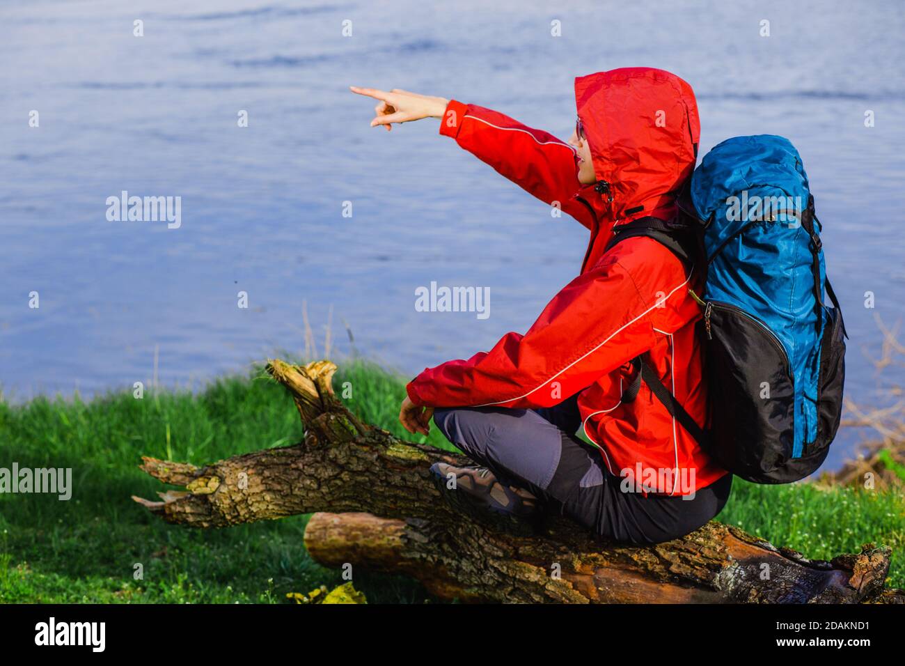 Turista con uno zaino, accoccolato su un ceppo vicino al fiume e punta alla distanza. Foto Stock