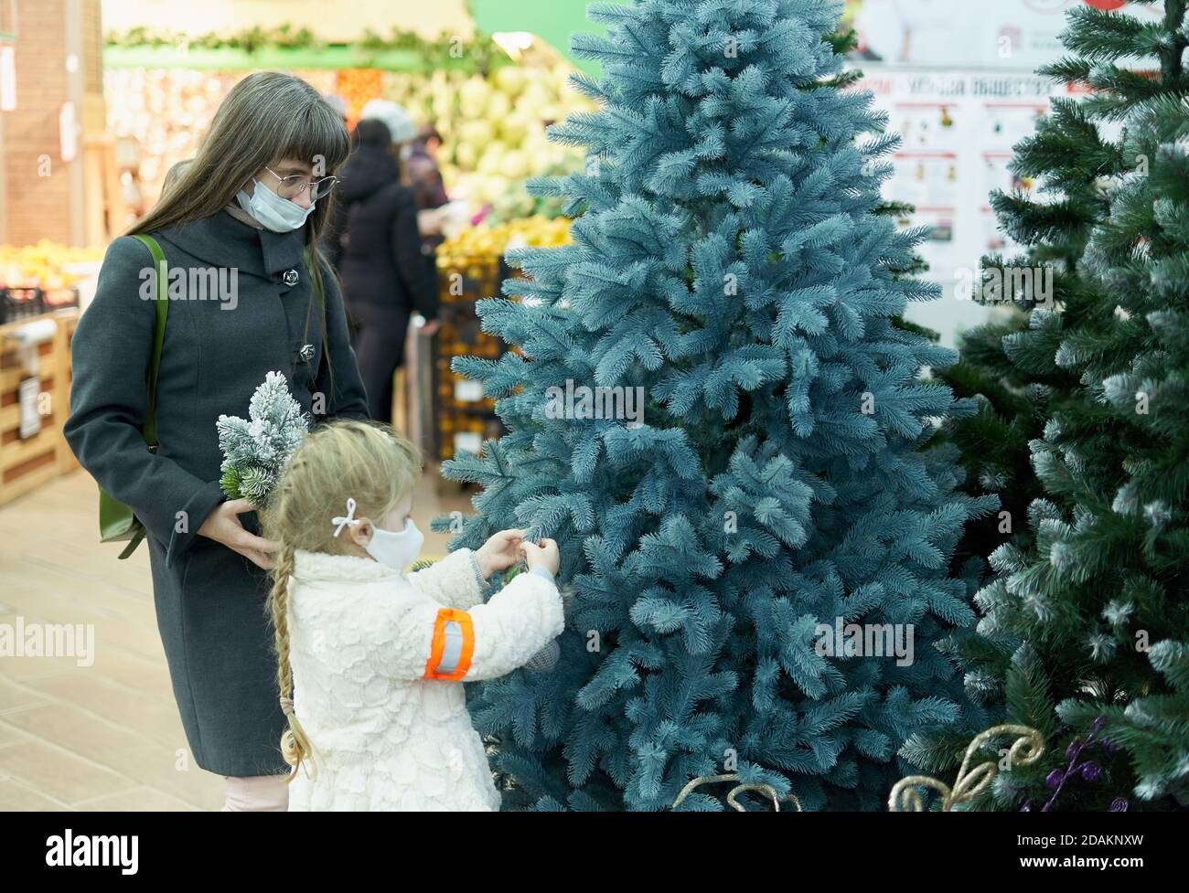 Giovane madre con un bambino scegliere un albero di Natale in PVC in un centro commerciale Foto Stock