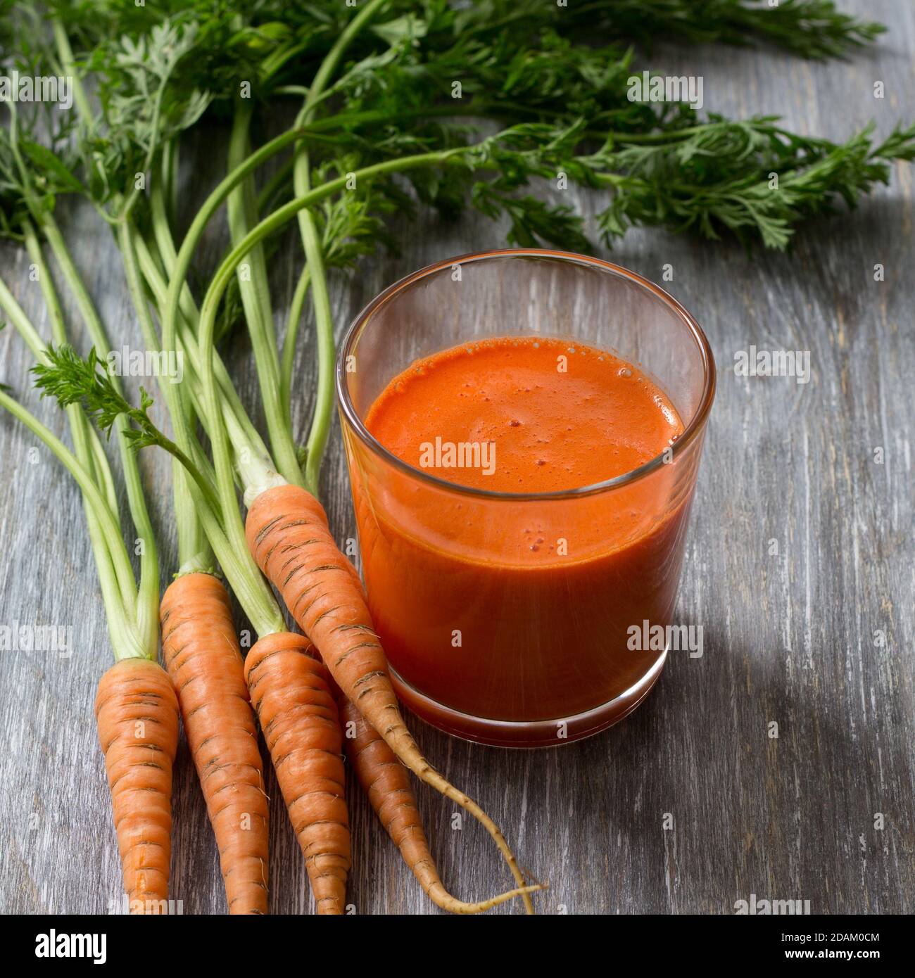 Succo di carote appena spremuto da una carota giovane in un bicchiere su un tavolo di legno, fuoco selettivo Foto Stock
