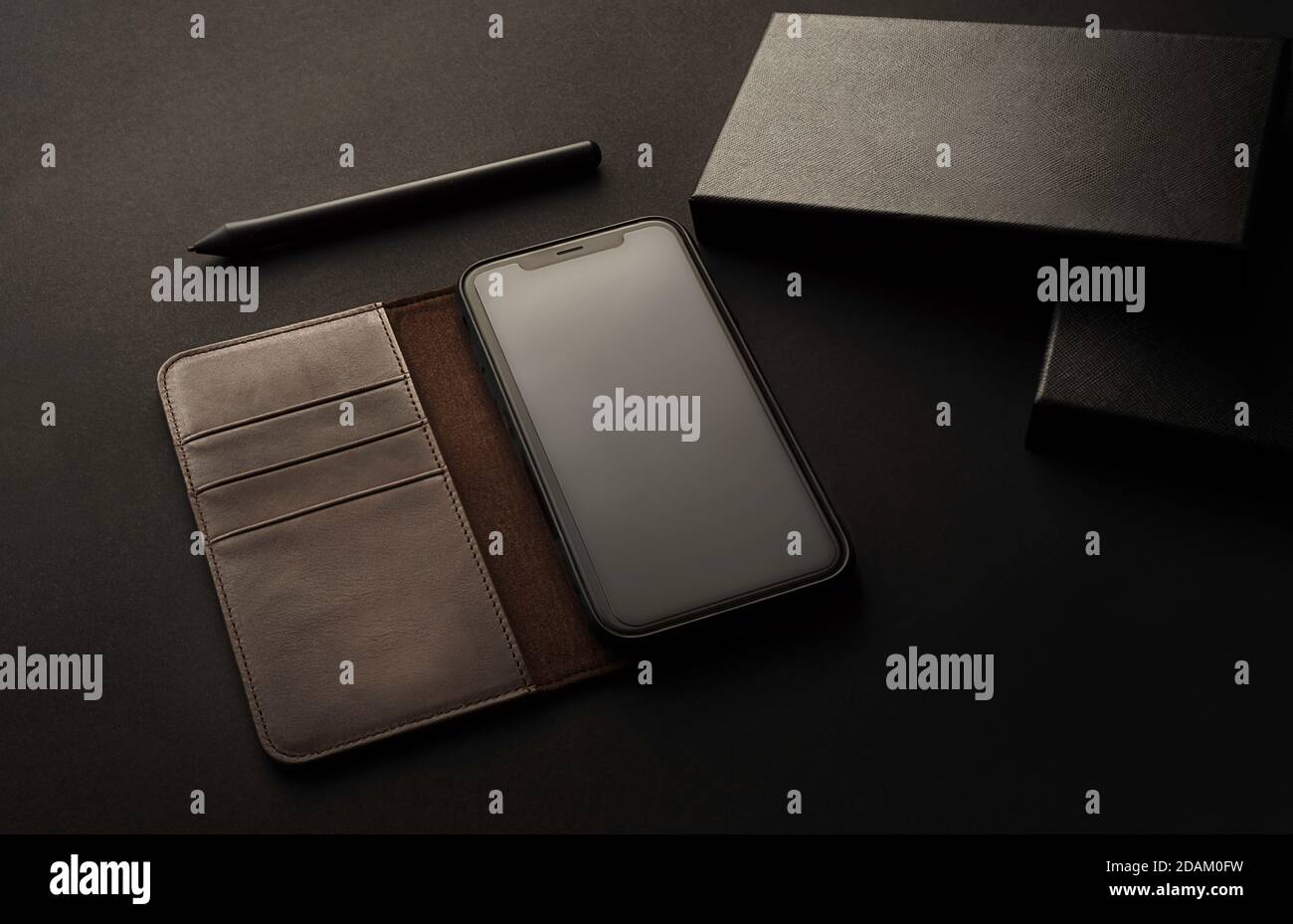Telefono cellulare con custodia e astuccio, custodia in pelle, morbida luce laterale sul tavolo da ufficio, elegante presentazione del prodotto con colori nero e grigio, ideale per m Foto Stock