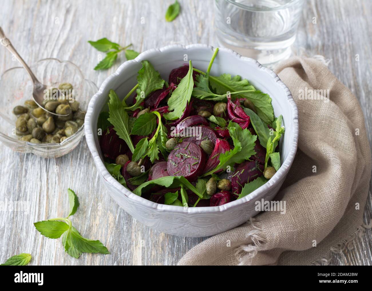 Insalata di barbabietole con cipolla rossa al forno, capperi, crescione, verdure e salsa vinaigrette. Cibo vegano sano. In una ciotola blu su un tavolo di legno Foto Stock