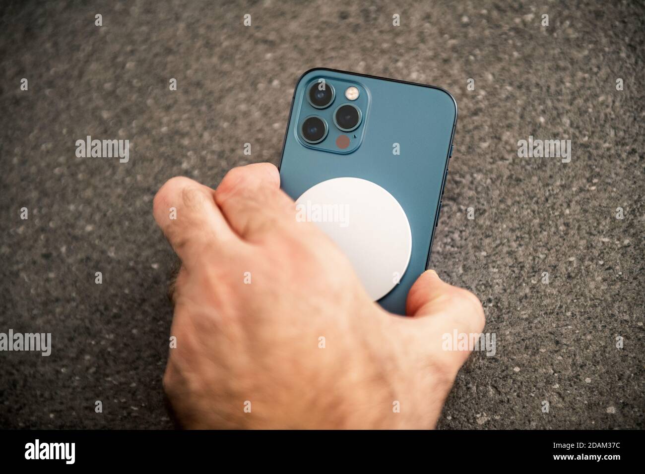 Parigi, Francia - Novembre 11, 2020: Uomo che posiziona dispositivo di ricarica MagSafe Wireless Charger l'ultimo modello di smartphone iPhone 12 Pro Max 5G di Apple computer primo piano di Pacific Blue Mobile Phone Device - sfondo in ceramica Foto Stock