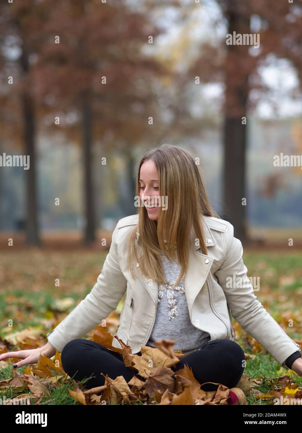 Giovane donna bionda seduta nel Parco Autunno con l'acero marrone Foglie Foto Stock