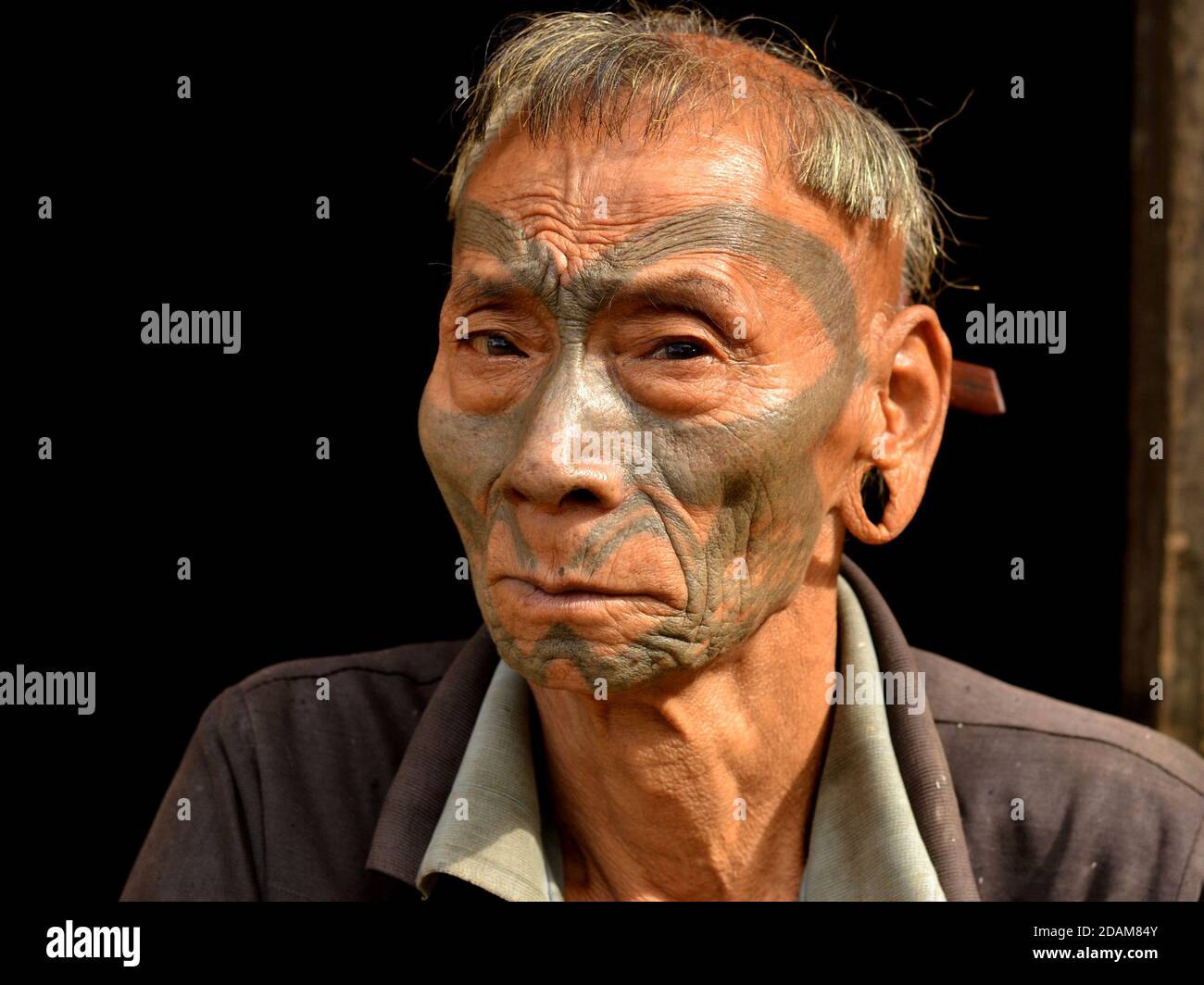 Vecchio guerriero indiano pensionato Konyak Naga e headhunter con gli occhi tristi, tatuaggio facciale tribale e distintive pose tradizionali di acconciatura per la macchina fotografica. Foto Stock