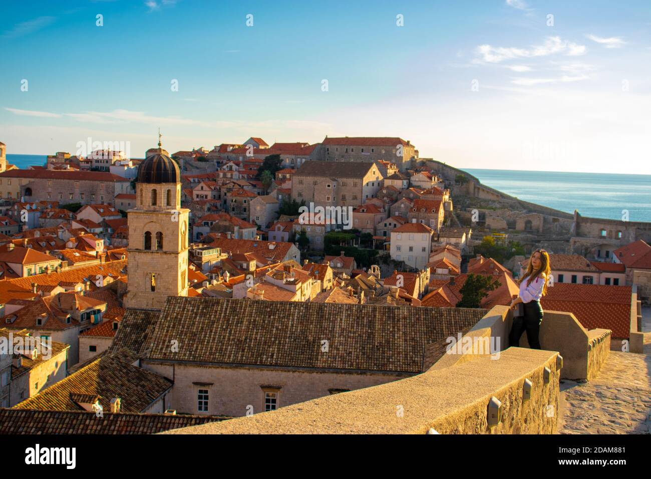 Bella brunetta che si erge sulle mura della città vecchia di Dubrovnik, piccole case e tetti che circondano tutta l'area antica. Chiesa campana Foto Stock