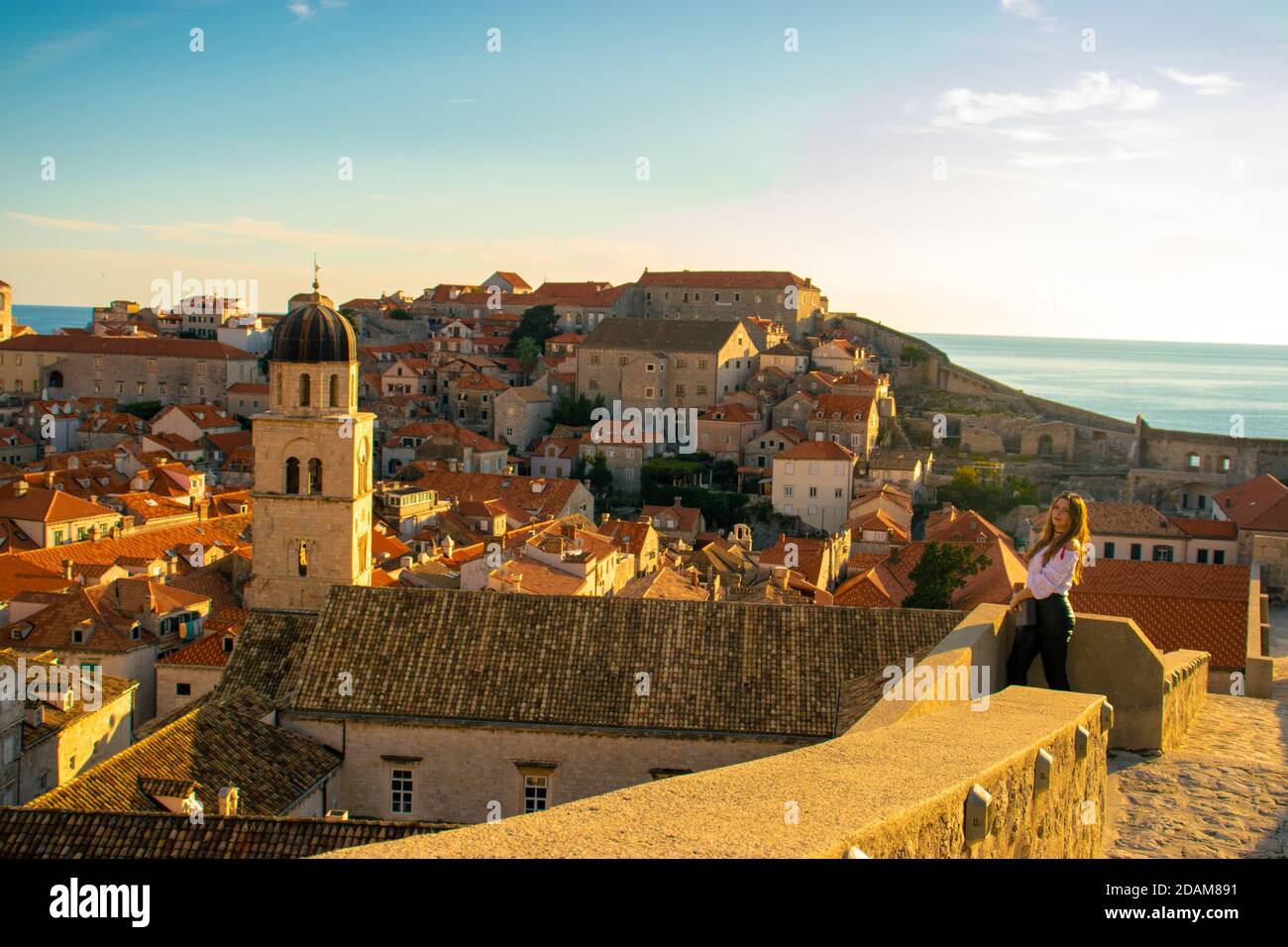 Bella brunetta che si erge sulle mura della città vecchia di Dubrovnik, piccole case e tetti che circondano tutta l'area antica. Chiesa campana Foto Stock