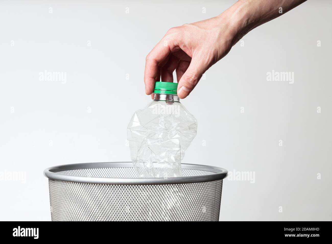 Mano gettando bottiglia vuota di plastica in una bomboletta di rifiuti Foto Stock