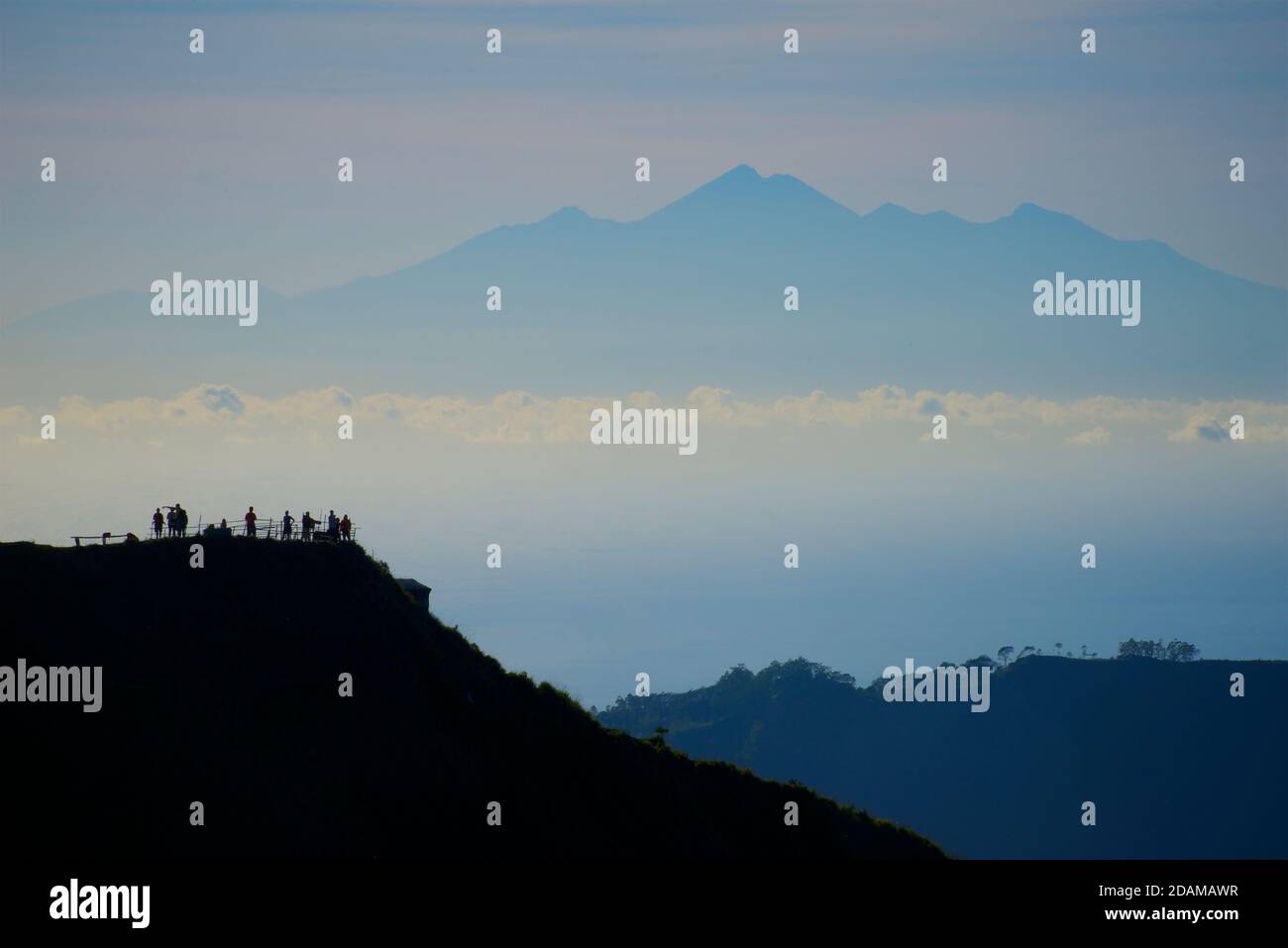 Monte Rinjani a Lombok visto da una salita del Monte Batur, Bali, Indonesia. Silhouette di escursionisti contro la fresca luce del mattino. Foto Stock