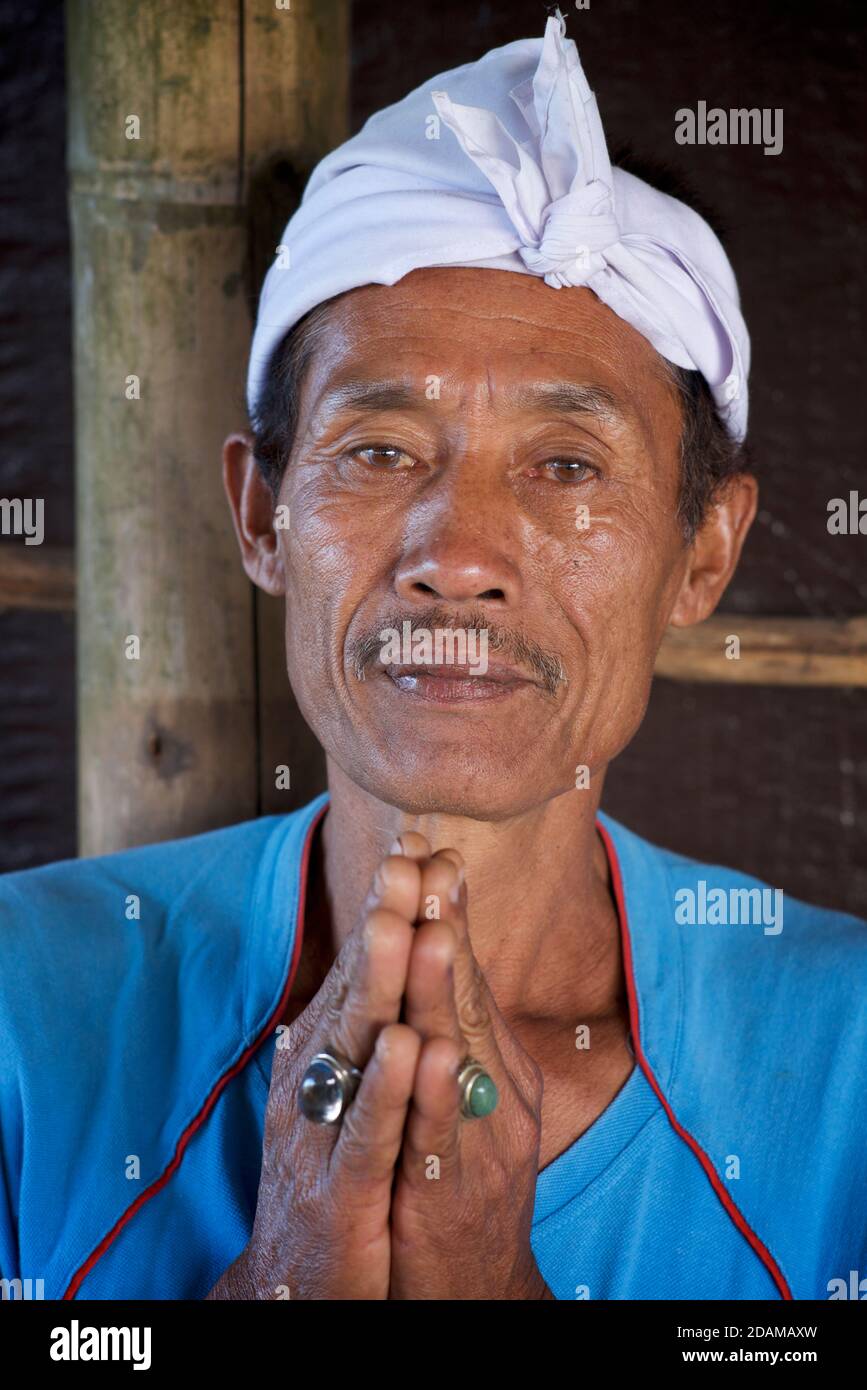 Ritratto di un uomo balinese con un capo bianco radioso che tiene un gesto di preghiera le emise le mani. Monte Batur, Bali, Indonesia Foto Stock