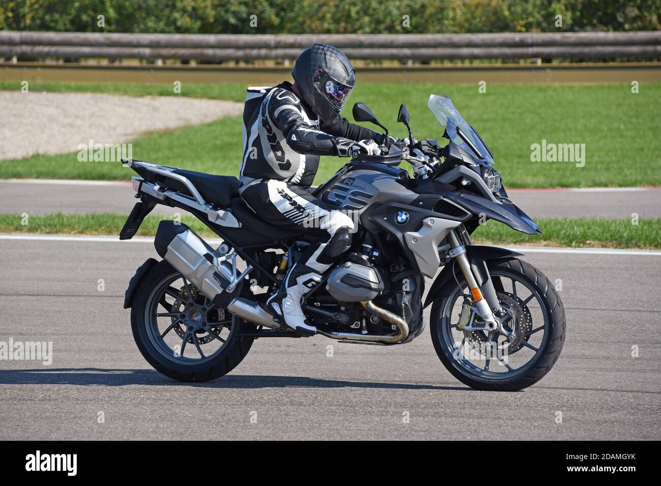 Persona in pelle piena e casco a cavallo di una moto BMW lungo una strada con vista laterale sotto il sole Foto Stock
