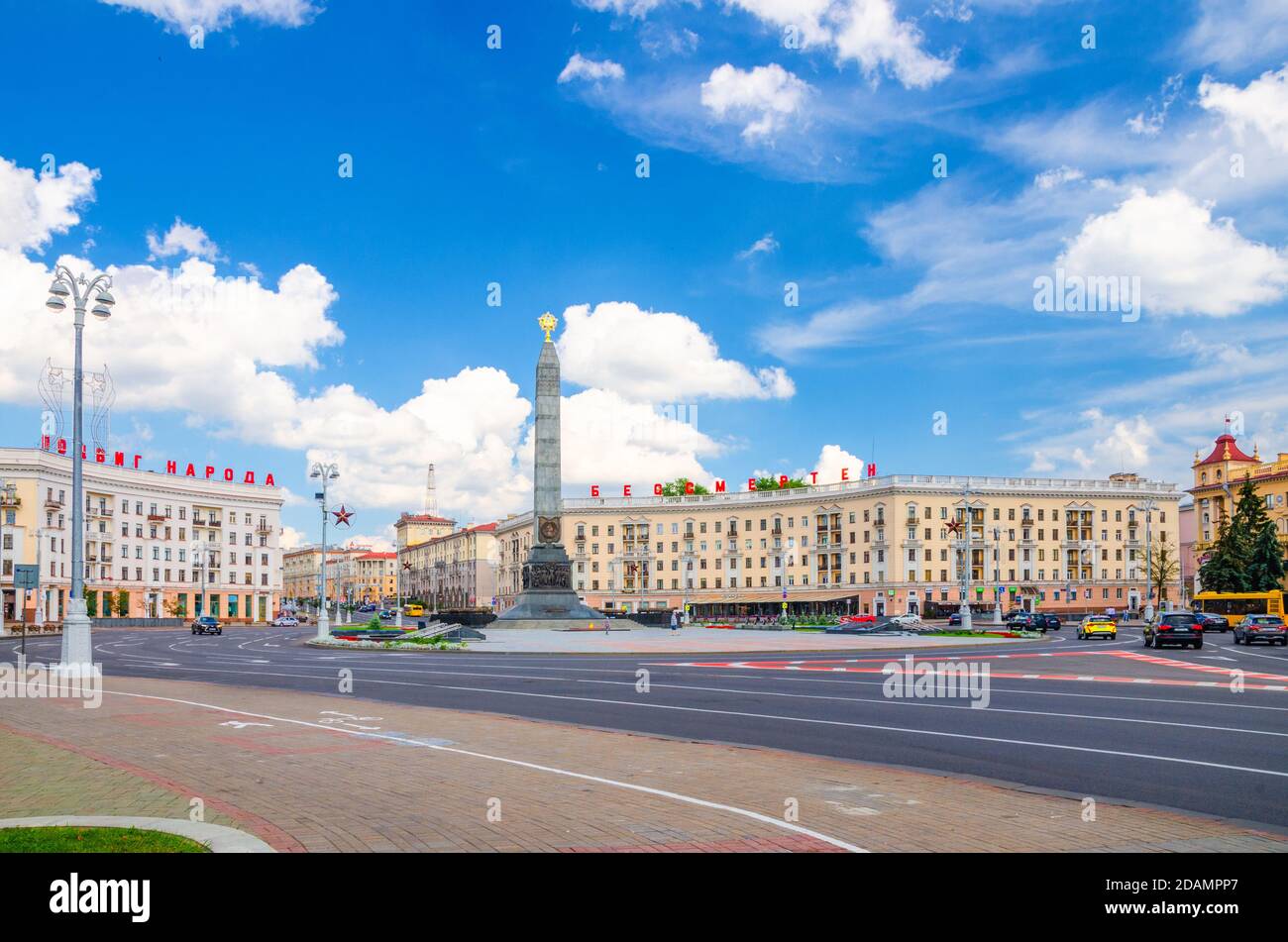 Minsk, Bielorussia, 26 luglio 2020: Piazza della vittoria nel centro della città con Granite Monumento della Vittoria, lettere rosse sugli edifici leggere l'atto eroico del popolo è immortale, cielo blu nuvole bianche giorno di sole Foto Stock