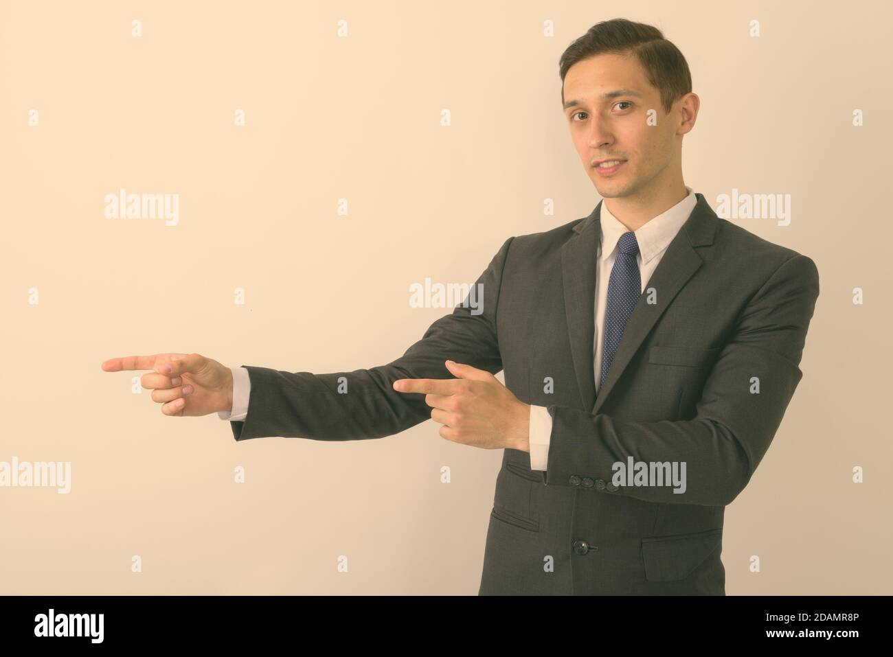 Studio di giovane bel uomo d'affari che mostra qualcosa mentre indica dita su sfondo bianco Foto Stock