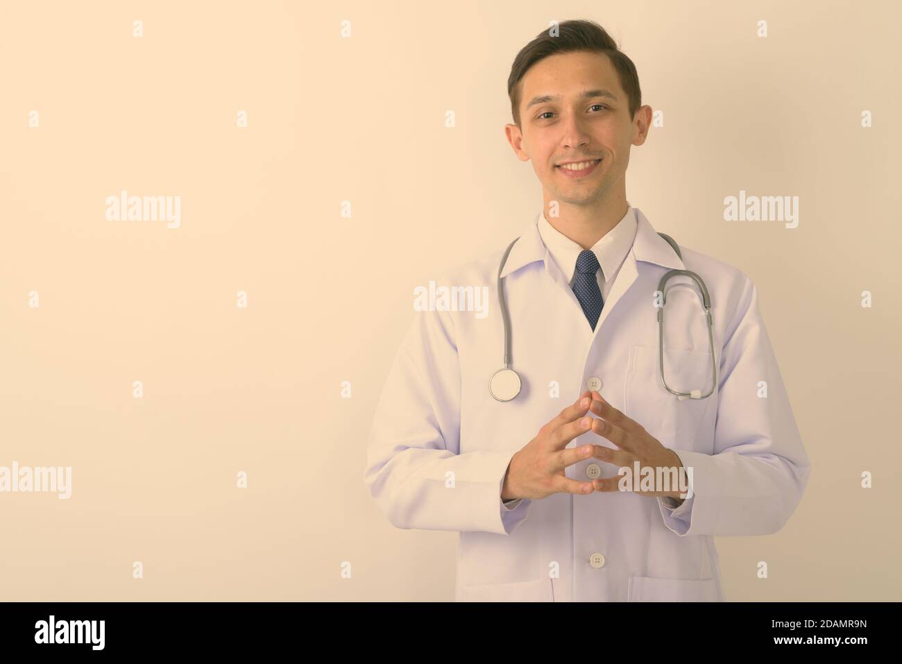 Studio shot del giovane uomo felice medico sorridente con le dita intrecciate insieme contro uno sfondo bianco Foto Stock