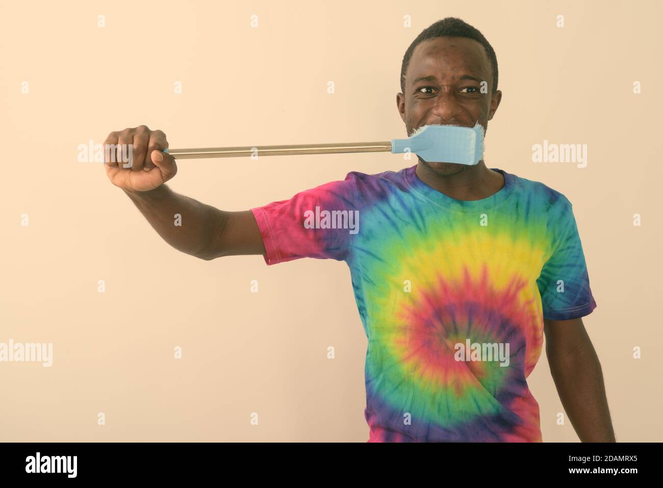 Studio di giovane uomo nero africano utilizzando grande pulizia spazzola per spazzolare i denti su sfondo bianco Foto Stock