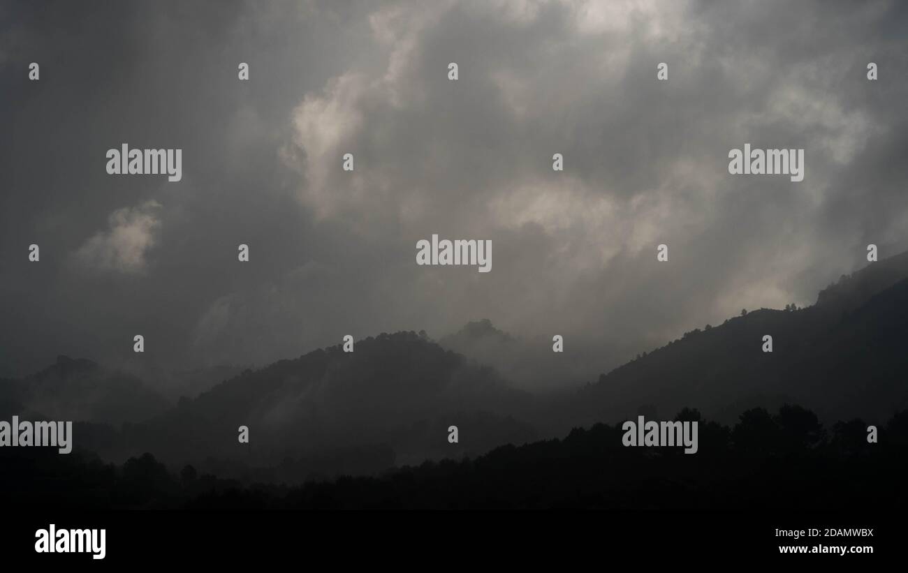 Nuvole basse e spesse e nebbia su colline scure poco prima alba Foto Stock