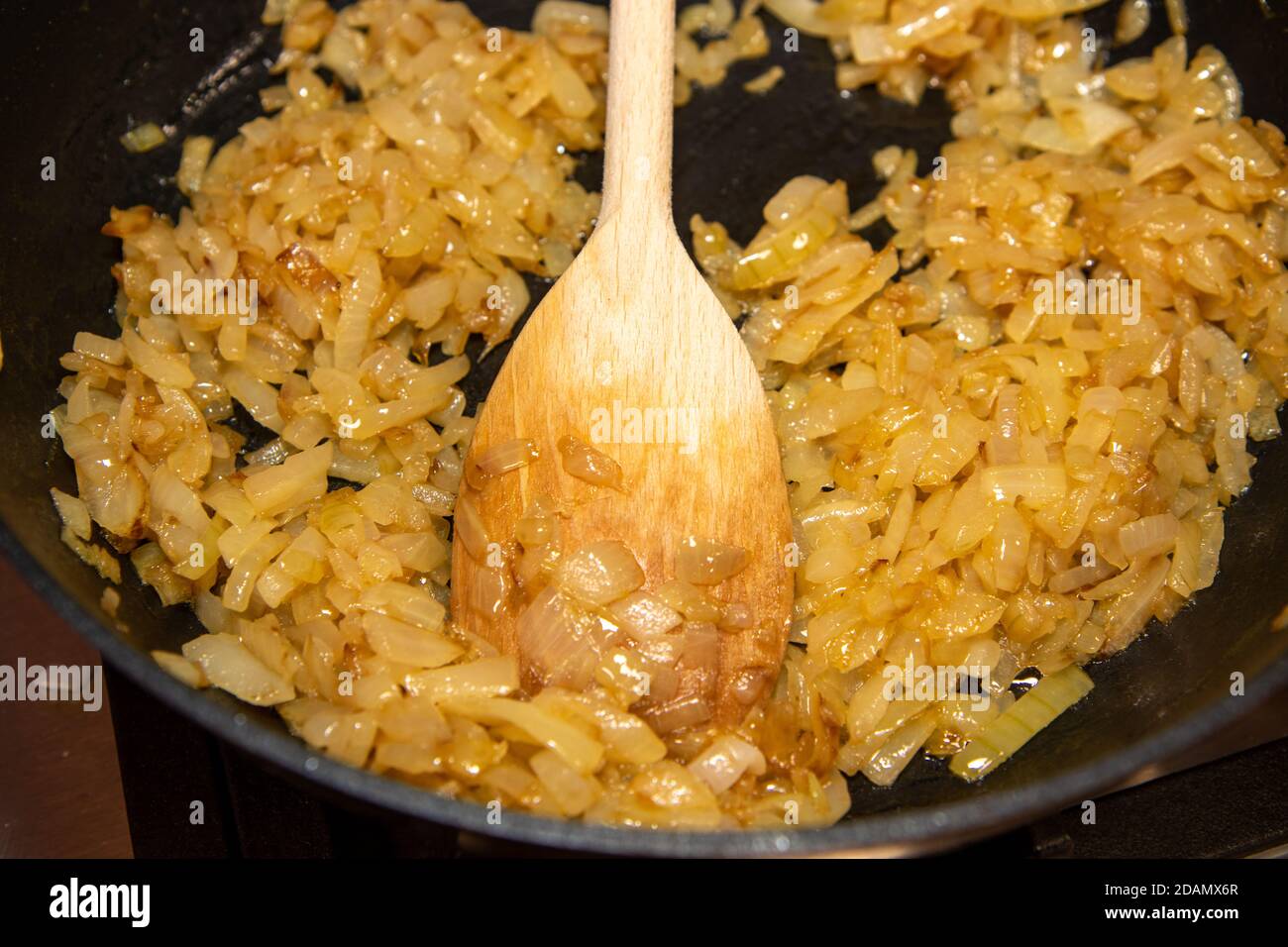 Le cipolle fritte cucinate in padella vengono spinte intorno con un cucchiaio di legno Foto Stock