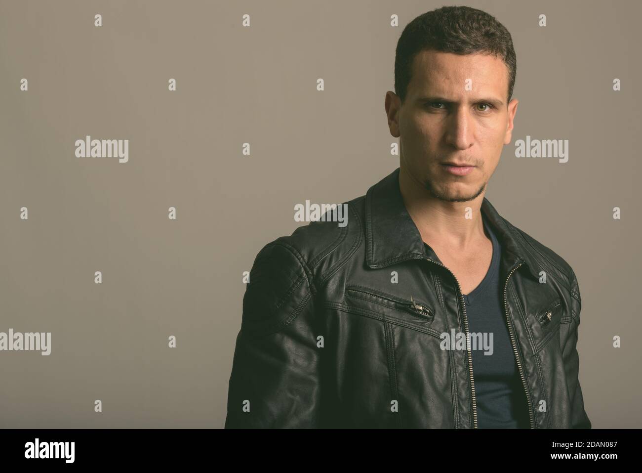 Studio shot di giovane uomo persiano muscoloso con giacca in pelle su sfondo grigio Foto Stock