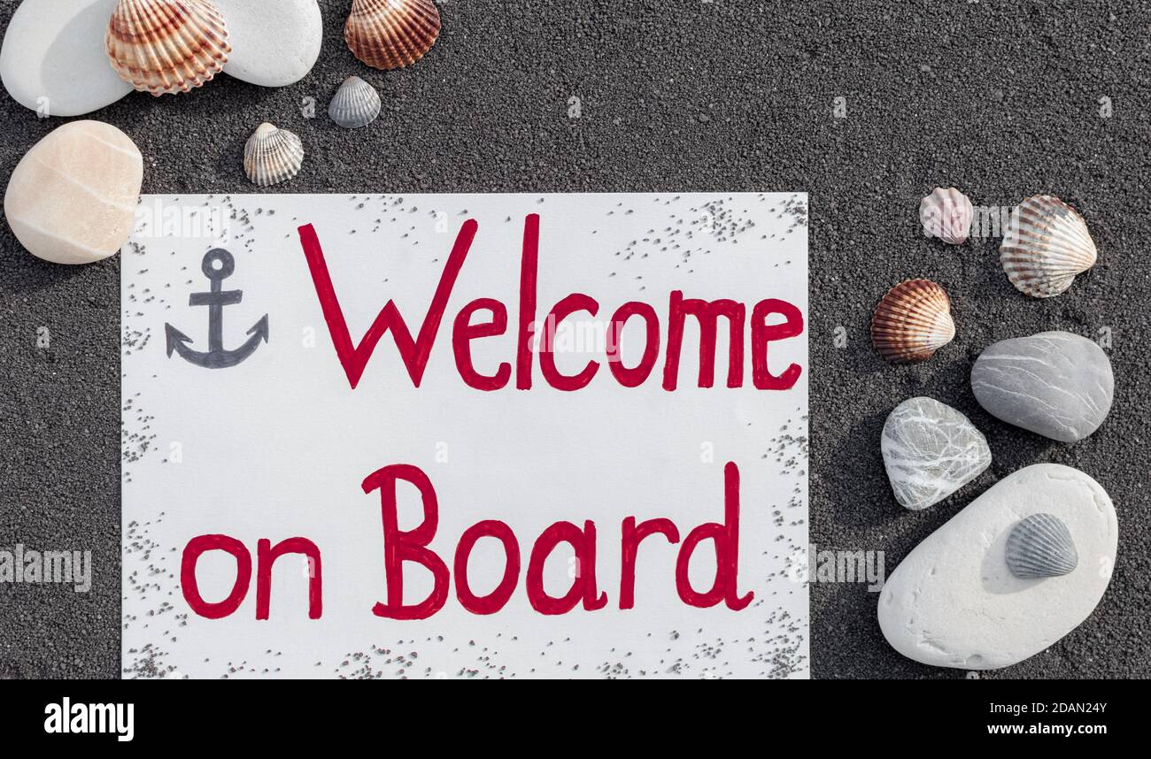 Messaggio di benvenuto a bordo su sfondo di sabbia nera con ciottoli e conchiglie. Foto Stock