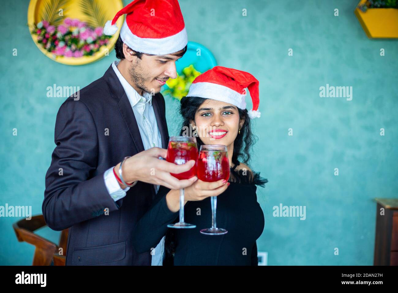 Festa di Natale, felice giovane coppia che indossa cappelli di santa cheering cocktail rossi bicchieri da bere a casa, spazio di copia. Amore, bonding, concetto di festa. Foto Stock