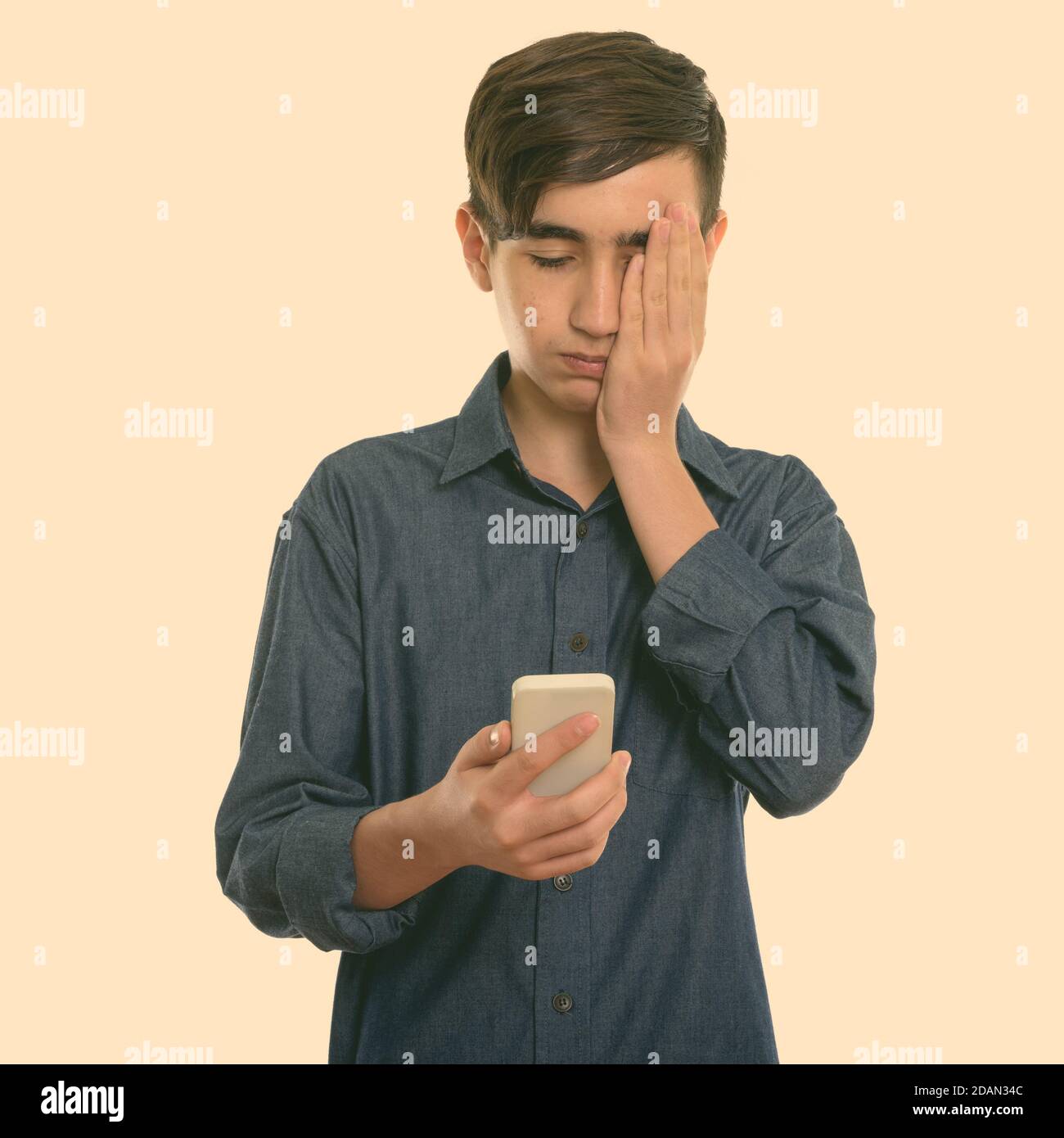 Studio girato di giovane ragazzo persiano stressato adolescente utilizzando il cellulare telefono mentre copra il viso Foto Stock