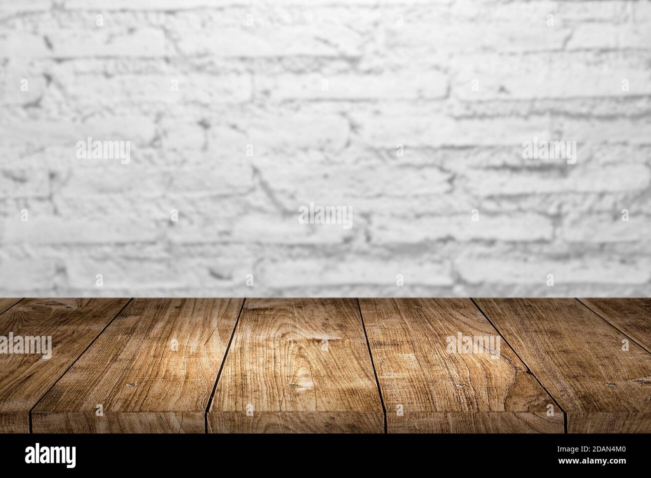 Bianco vecchio muro di mattoni con tavolo in legno in primo piano per il prodotto montaggio sfondo pubblicitario. Foto Stock