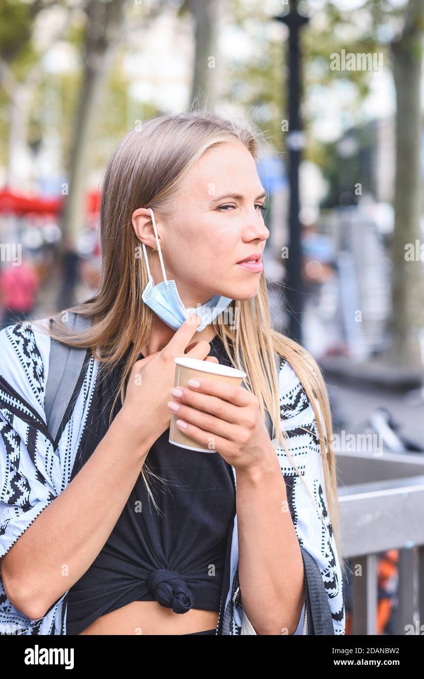 ritratto verticale di un bel modello femminile biondo che rimuove la maschera bere caffè e guardare a destra Foto Stock