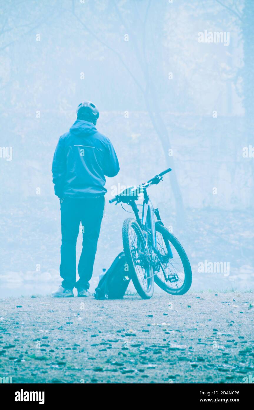 lone uomo in piedi vicino alla sua bicicletta di fronte ad un lago in una mattina foggy, riposante Foto Stock