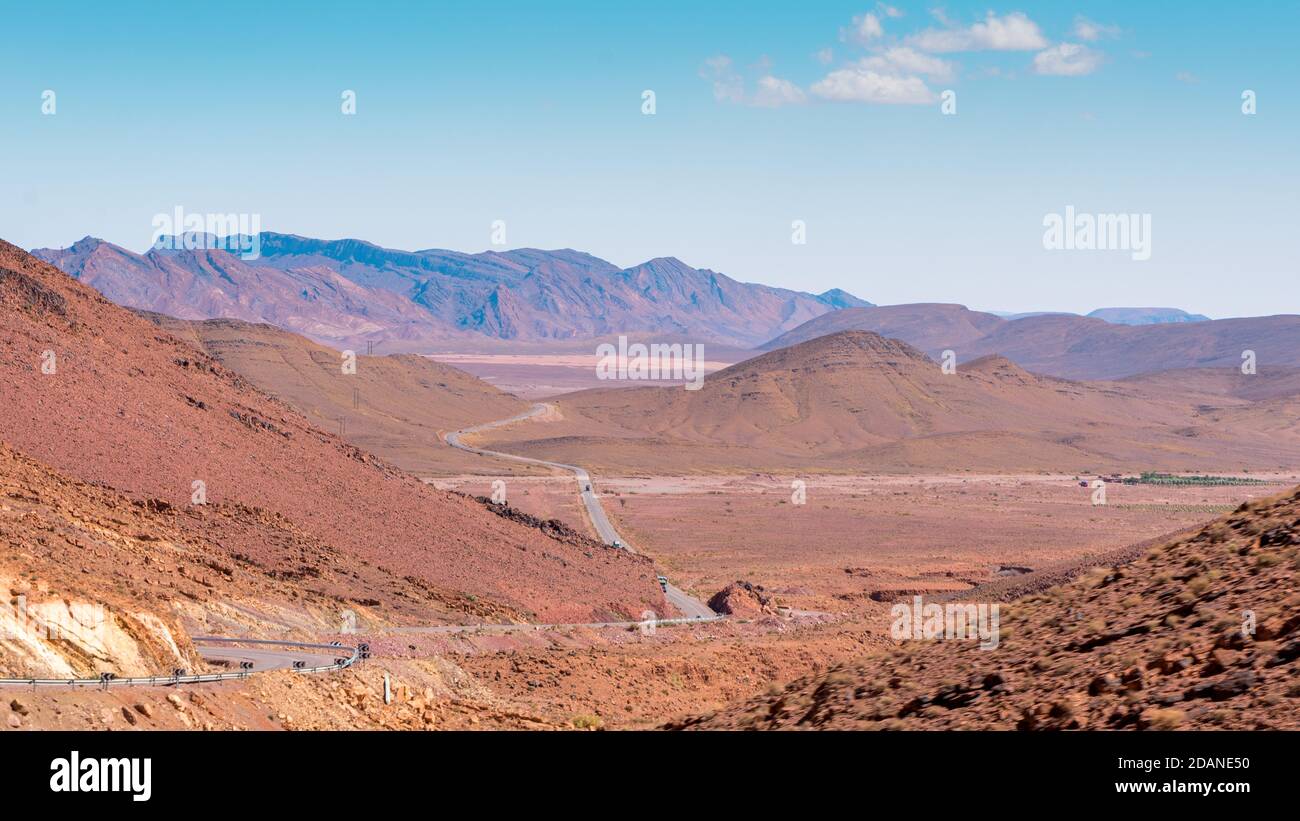 Paesaggio ultraterreno con montagne e terra rossastra e strada infinita che li attraversa. Alto Atlante, Marocco. Foto Stock