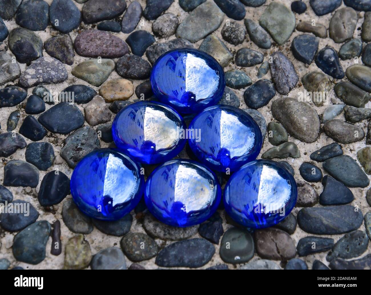 Piccolo triangolo di perline di vetro blu iridescenti isolato su uno sfondo di pietra ciottolosa. Foto Stock