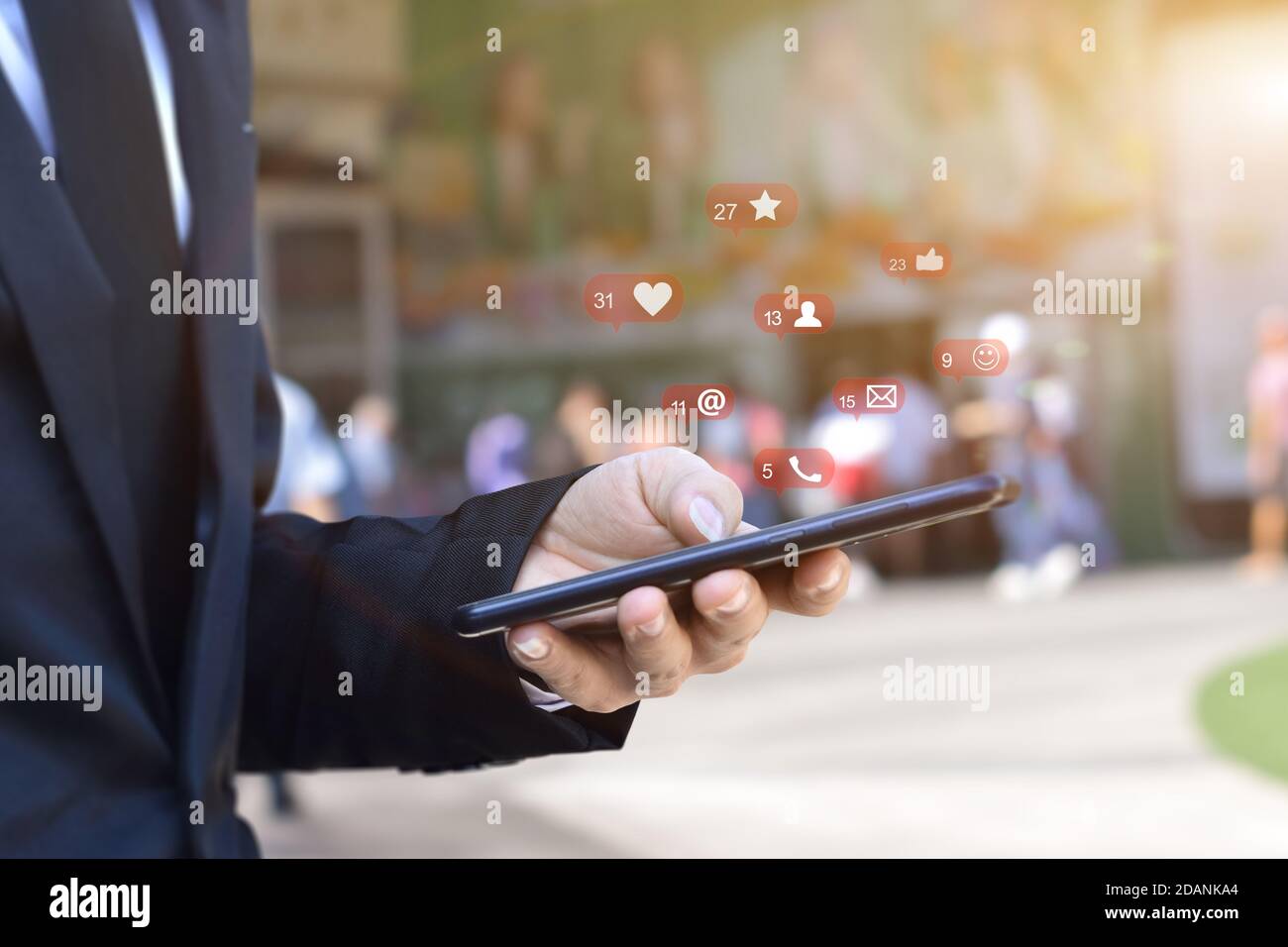 Primo piano di un uomo d'affari che utilizza uno smartphone mobile con icone dei social media sullo sfondo sfocato della stazione aeroportuale. Business, tecnologia o social networ Foto Stock