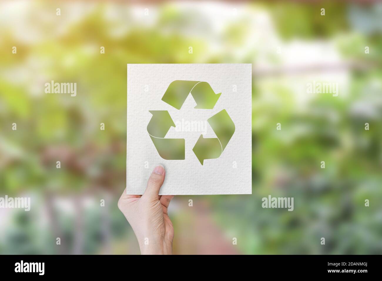 Mano che tiene carta tagliata con il logo riciclare su sfondo verde sfocato natura. Foto Stock
