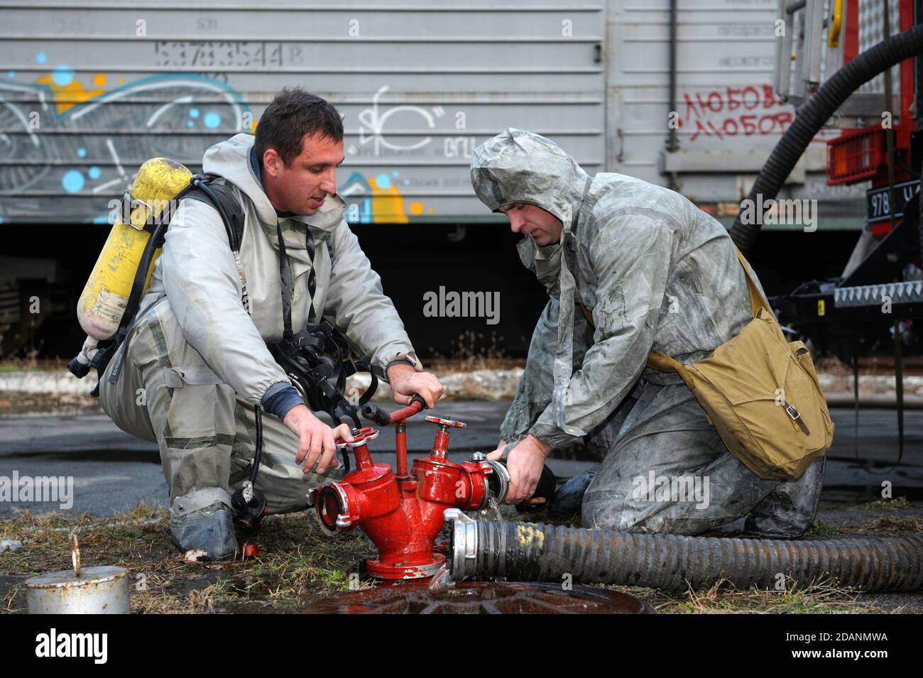 Formazione del team di soccorso sulla decontaminazione chimica: Soccorritore in un gruppo protettivo che gira una valvola di un idrante antincendio Foto Stock