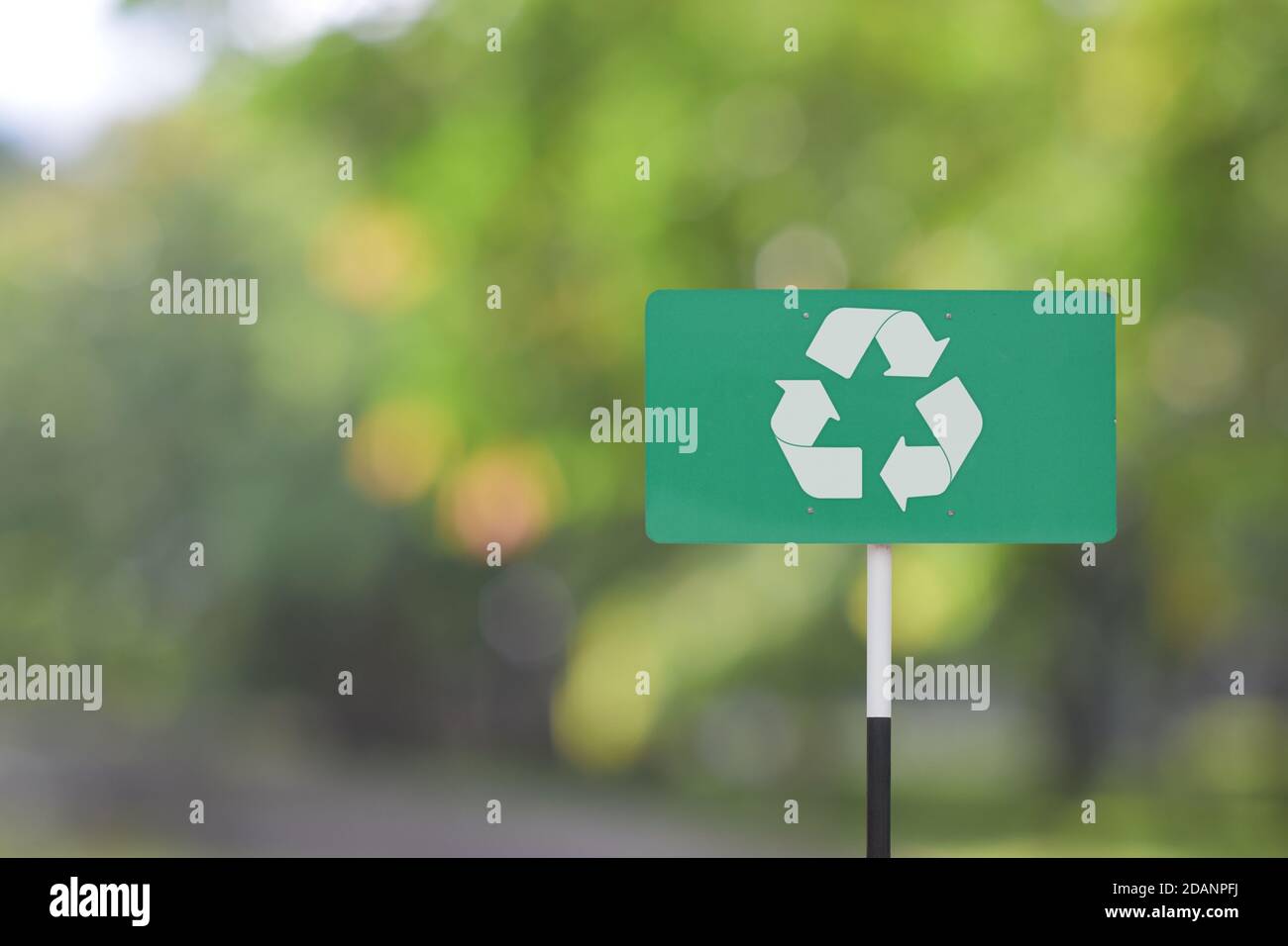 Un cartello stradale con il simbolo del logo di riciclo su sfondo verde sfocato. Foto Stock