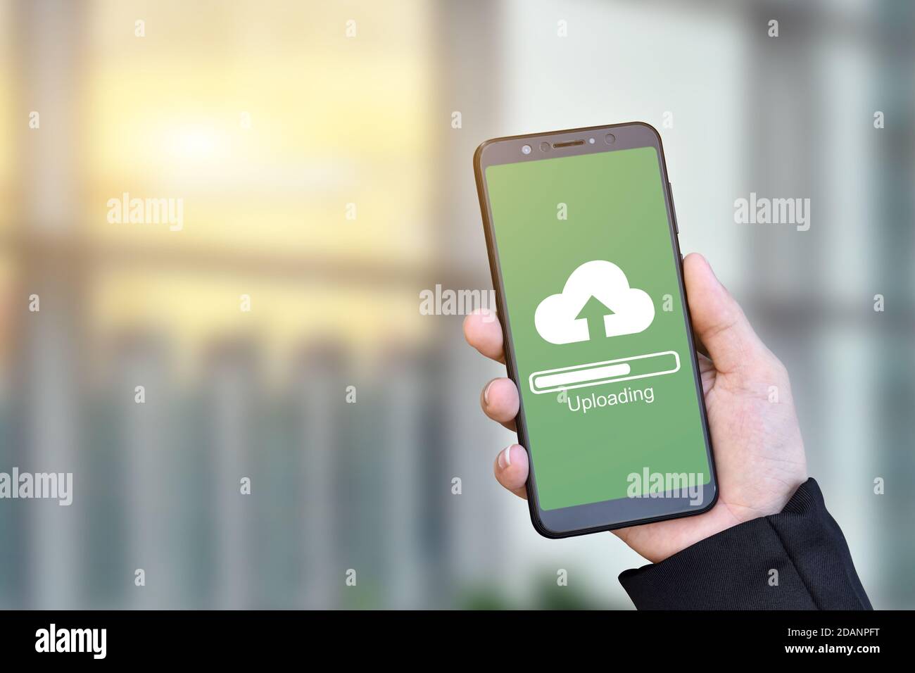 Primo piano di un uomo d'affari che tiene lo smartphone mobile con caricamento sul cloud per archiviare i dati sul server. Foto Stock